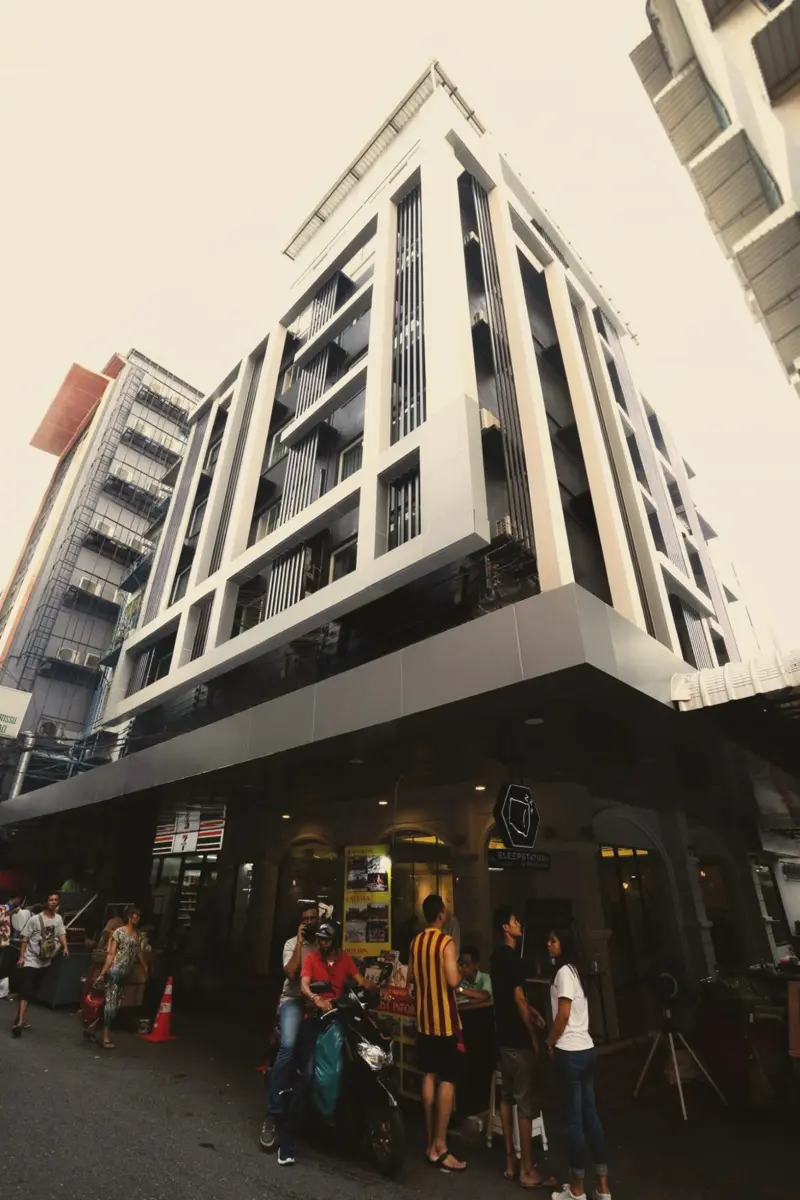 Sleepstation hotel building on a busy Pratunam street corner, with the hexagon sign above the entrance